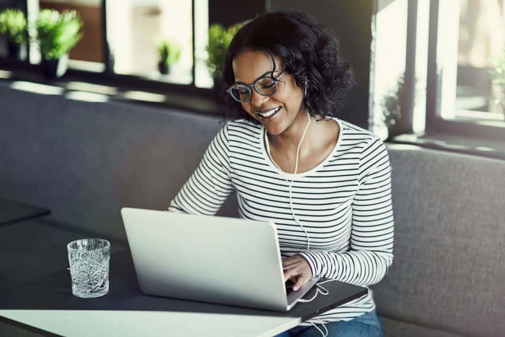woman in black and white striped shirt blogging from a gray cafe booth