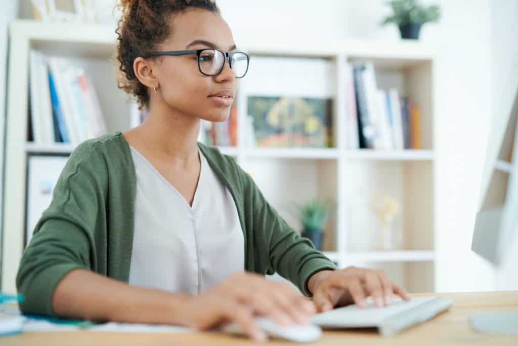 young woman wearing a green cardigan working on a desktop computer in a home office
