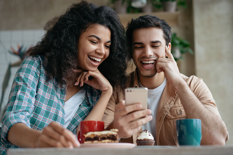 two people smiling at phone while eating baked goods