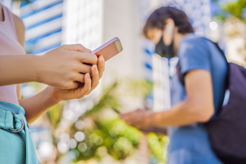 person using phone with another wearing mask in the background