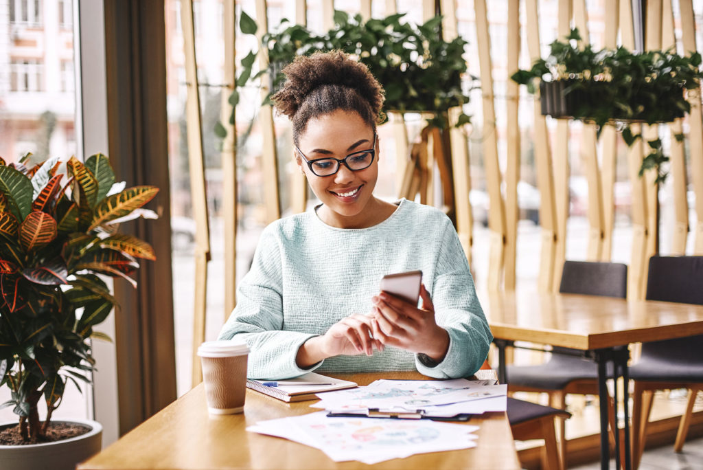 woman using a mobile phone in an office surrounded by papers with graphs on them